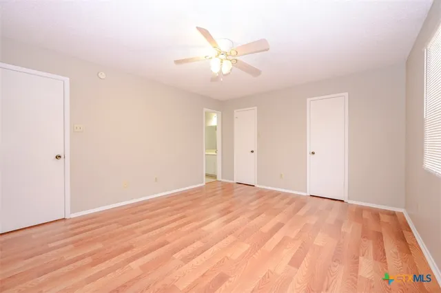 a view of an empty room with wooden floor and a ceiling fan