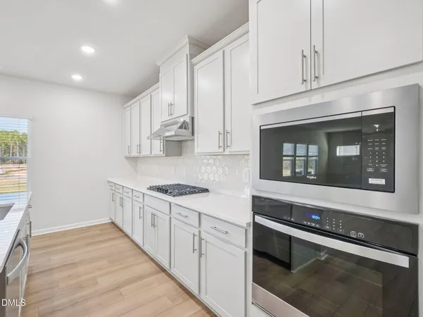 a large kitchen with kitchen island a sink a stove a refrigerator and white cabinets with wooden floor