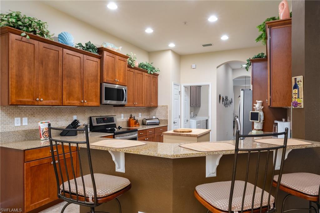26479 Lucky Stone Road, Unit 202 Bonita Springs, FL 34135 - Photo 17 of 38 a kitchen with stainless steel appliances granite countertop a stove a sink a microwave a dining table and chairs
