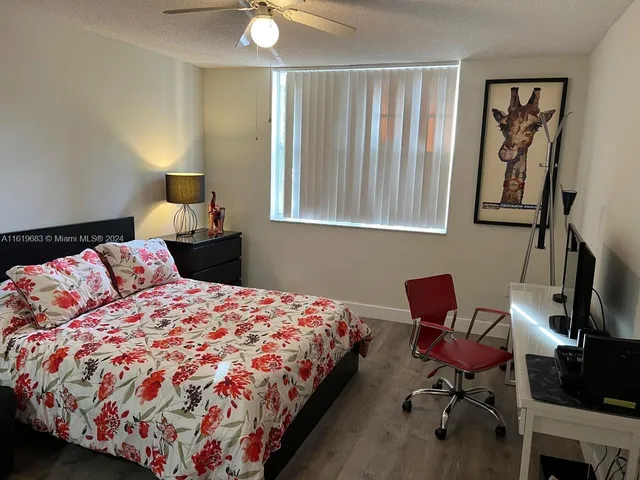 a bedroom with a bed a chair and potted plant on the dresser