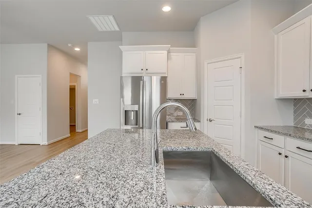 a kitchen with stainless steel appliances granite countertop a refrigerator a sink and white cabinets