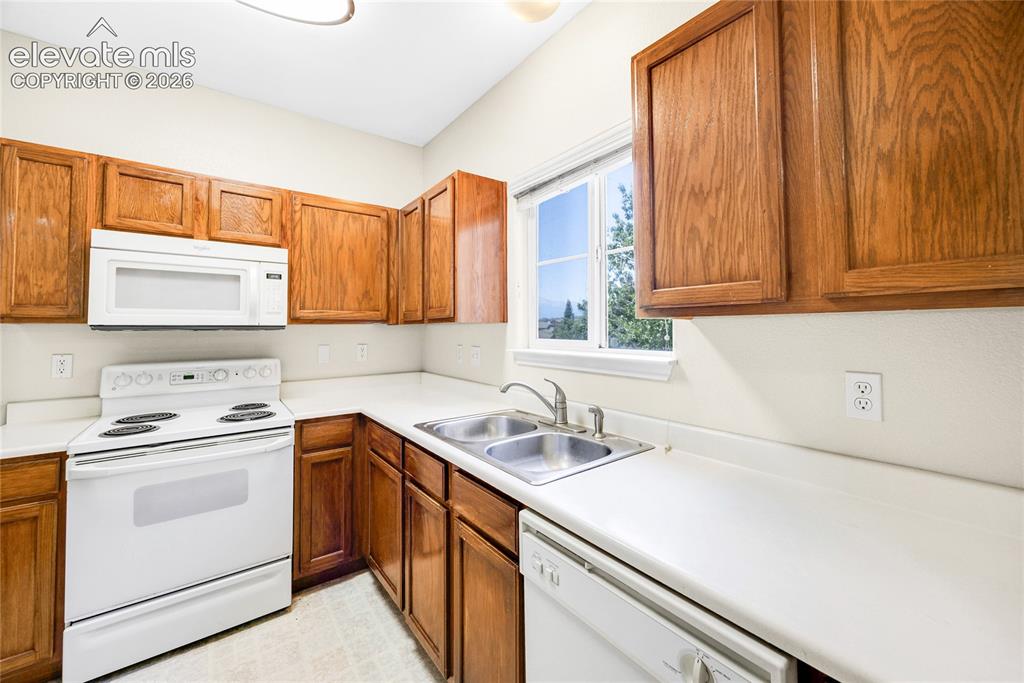 3864 Riviera Grove, Unit 102 Colorado Springs, CO 80922 - Photo 9 of 24 Kitchen featuring wood cabinetry, white countertops, a double basin stainless steel sink, a white electric range, and a built-in white microwave