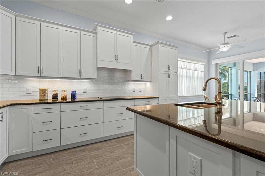 5916 Antigua Way Naples, FL 34113 - Photo 6 of 50 Kitchen with sink, dark stone countertops, white cabinets, ceiling fan, and backsplash