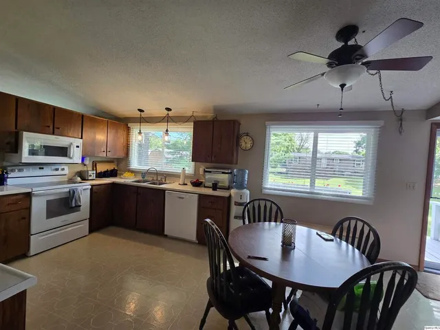 a kitchen with stainless steel appliances granite countertop a stove a refrigerator a kitchen island a sink dishwasher a dining table and chairs with wooden floor