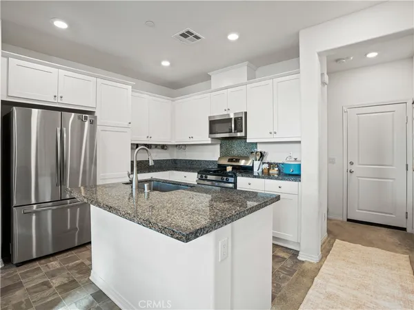 a kitchen with kitchen island granite countertop a refrigerator a sink a stove a microwave and island