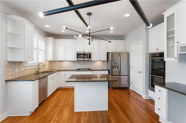 a large kitchen with stainless steel appliances granite countertop a refrigerator a stove a sink and white cabinets with wooden floor