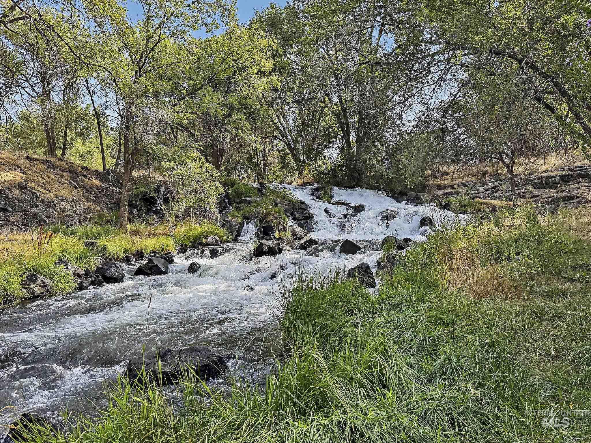 6900 West Charters Lane Melba, ID 83641 - Photo 45 of 49 Natural waterfall feature with a rocky stream bed, surrounded by lush green foliage and mature trees