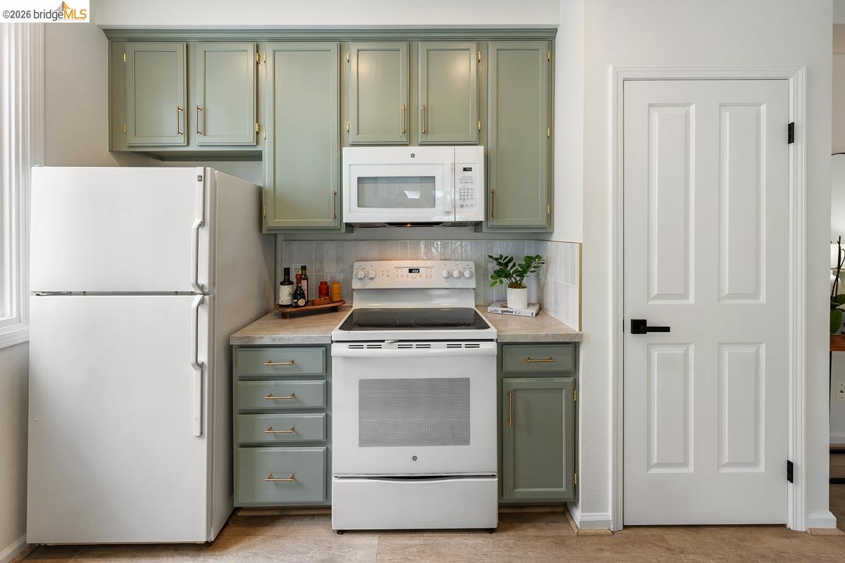 2029 Channing Way, Unit 3D Berkeley, CA 94704 - Photo 21 of 54 Kitchen area featuring green cabinetry, white appliances including a refrigerator and range with an over-the-range microwave, and a light-toned countertop