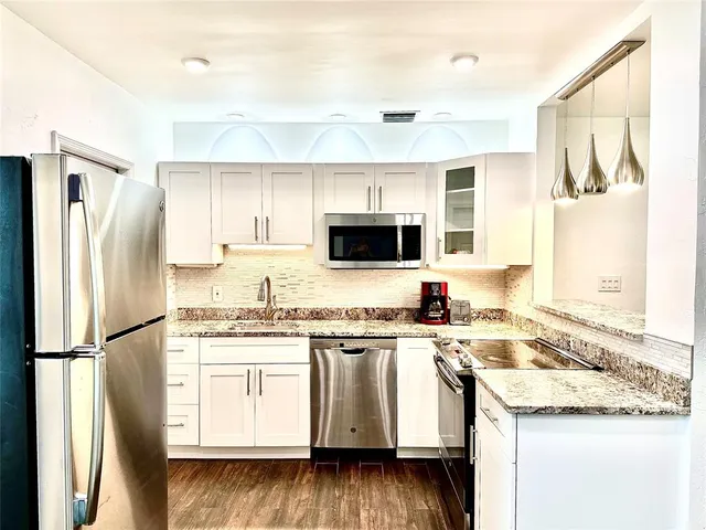 a kitchen with stainless steel appliances granite countertop a refrigerator a stove a sink and white cabinets with wooden floor