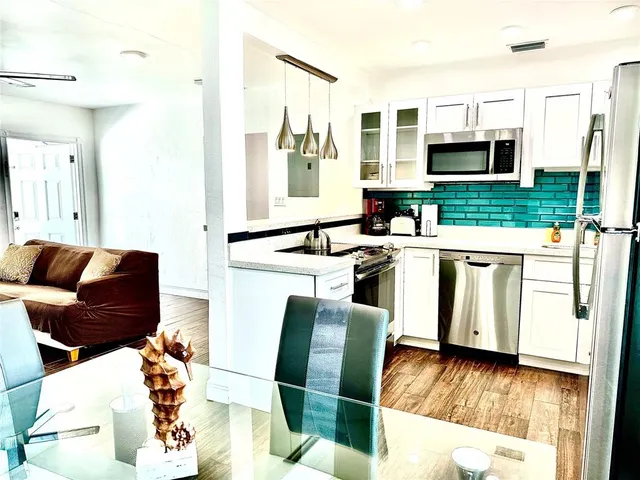 a living room with stainless steel appliances furniture a fireplace and a kitchen view