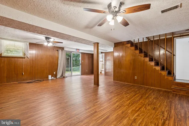 a view of an empty room with wooden floor and a ceiling fan