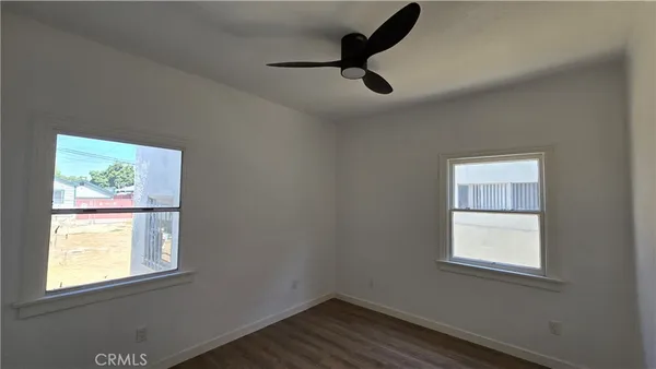 an empty room with wooden floor fan and windows