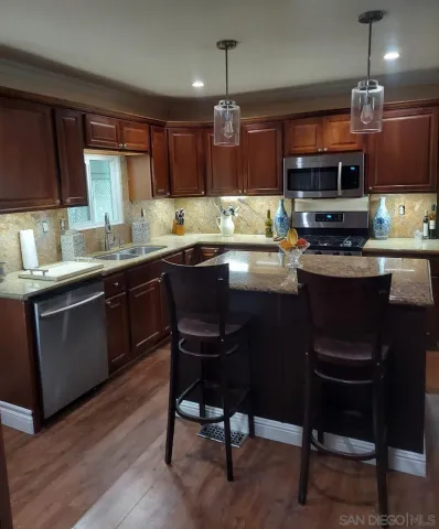 a kitchen with kitchen island granite countertop a sink a counter space stainless steel appliances and cabinets