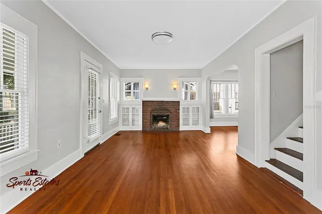 a view of an empty room with wooden floor fireplace and a window