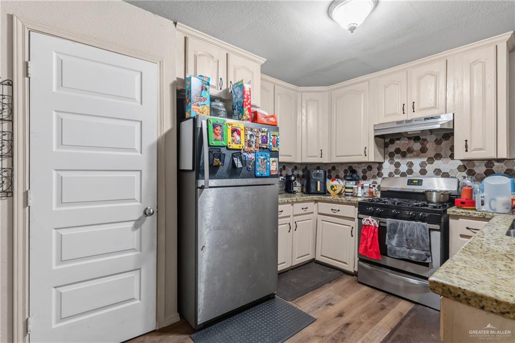 29246 26th Road San Benito, TX 78586 - Photo 6 of 23 Kitchen featuring upper and lower cabinetry, wood-finish flooring, a stainless steel range with a ventilation hood, and a hexagonal tile backsplash
