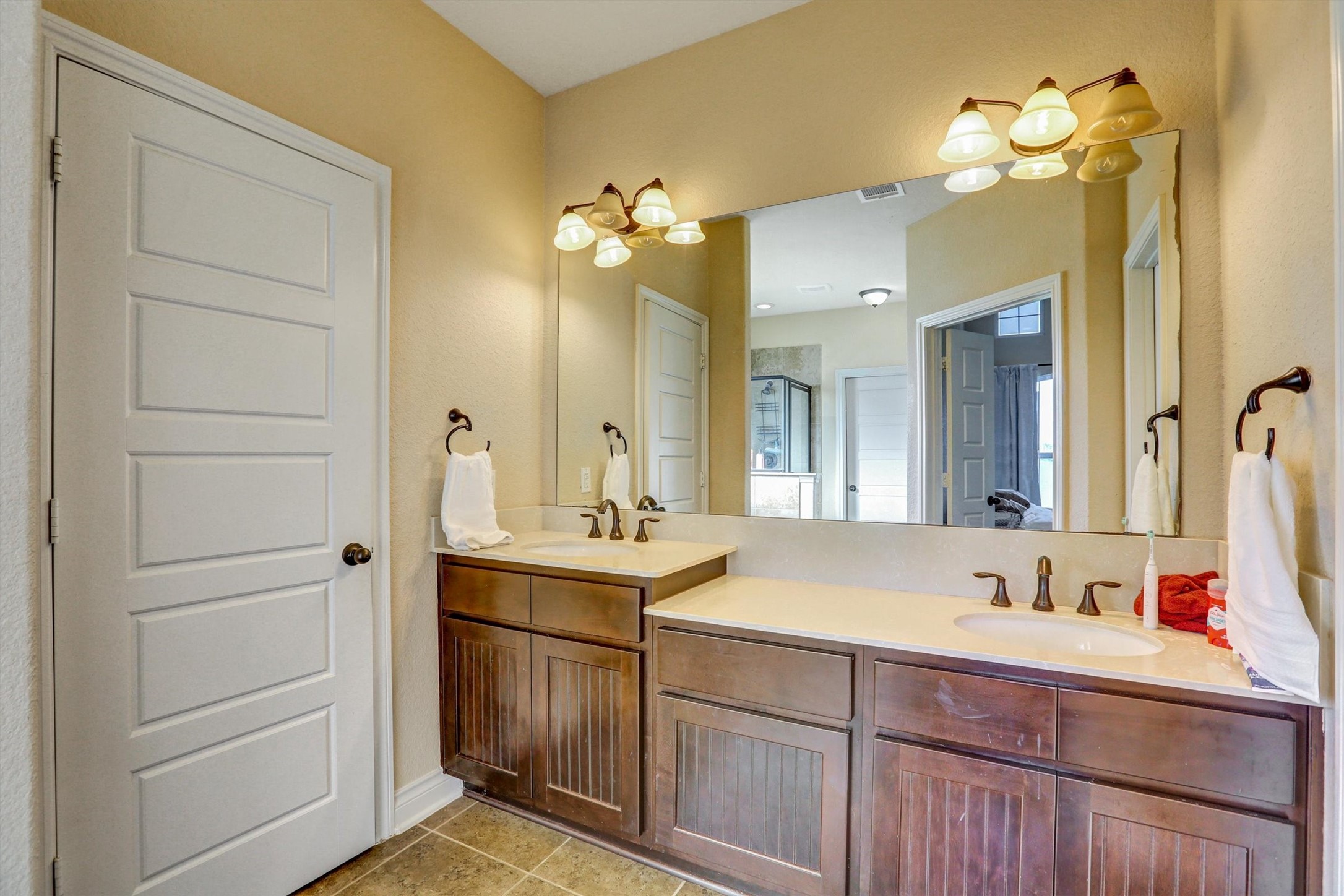 8131 Brinkmeyer Road Needville, TX 77461 - Photo 39 of 49 Spacious bathroom featuring a double vanity with rich wood cabinetry, elegant fixtures, and a large mirror, providing ample space and style.