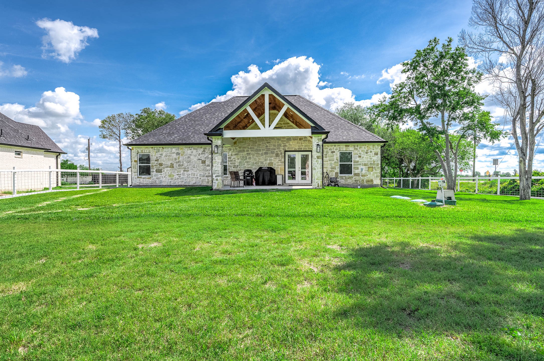 8032 Short Road Needville, TX 77461 - Photo 32 of 50 Charming stone home with a spacious backyard, covered patio, and expansive green lawn, creating the perfect setting for outdoor entertaining, relaxing, and everyday enjoyment.
