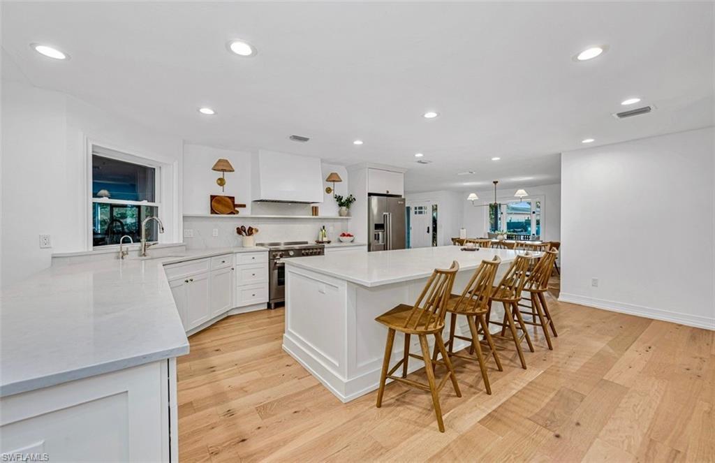 4870 Whispering Pine Way Naples, FL 34103 - Photo 4 of 43 a large white kitchen with white cabinets a sink dishwasher and a stove with wooden floor