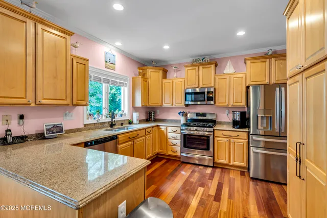 a kitchen with stainless steel appliances granite countertop a refrigerator a sink dishwasher a stove and white countertops with wooden floor