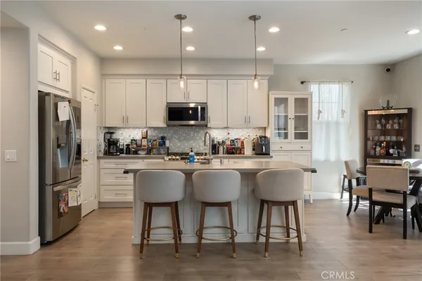 a kitchen with stainless steel appliances granite countertop a refrigerator a stove top oven a sink dishwasher a dining table and chairs with wooden floor