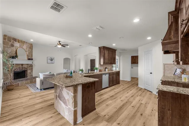 a open kitchen with kitchen island a stove a sink dishwasher and a fireplace with wooden floor