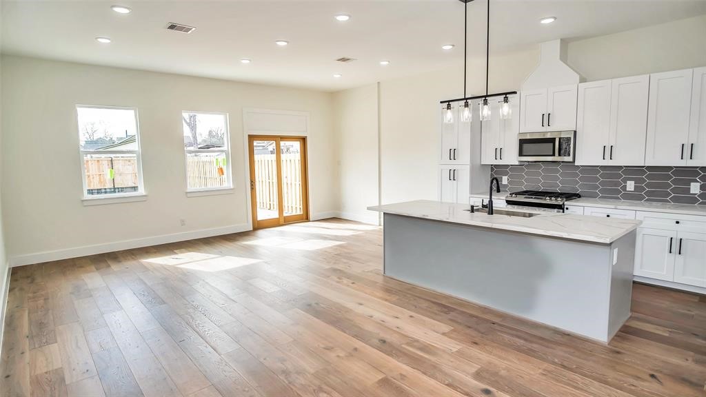 1508 Weiss Street Houston, TX 77009 - Photo 3 of 16 a kitchen with granite countertop a stove a sink and white cabinets with wooden floor next to windows