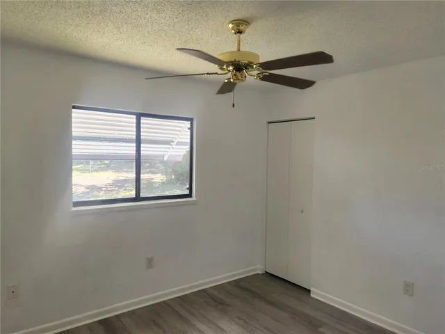 an empty room with wooden floor fan and windows