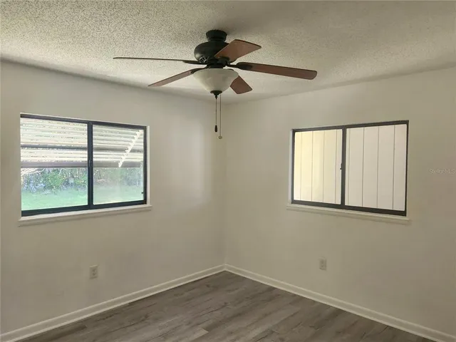 an empty room with wooden floor fan and windows