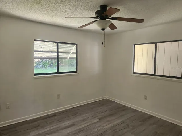 an empty room with wooden floor ceiling fan and windows