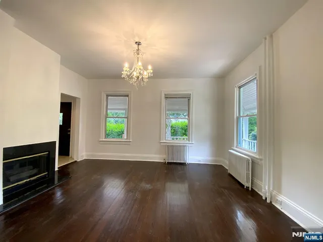 an empty room with wooden floor chandelier and windows