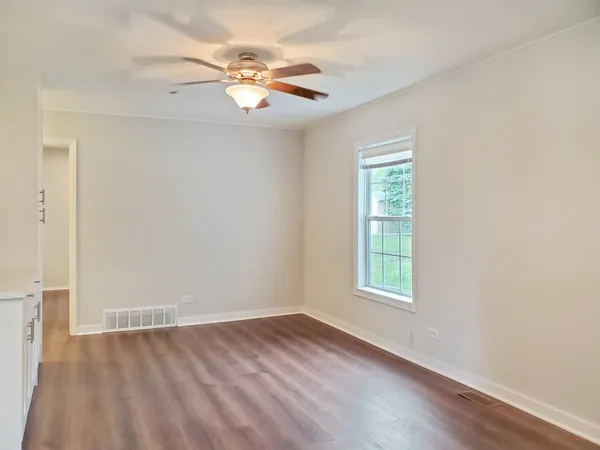an empty room with wooden floor chandelier fan and windows