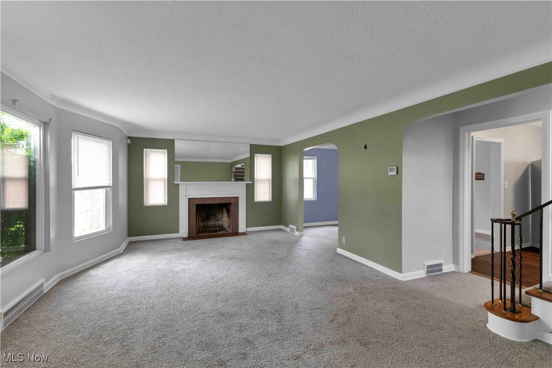 3385 Rosedale Road Cleveland, OH 44112 - Photo 10 of 40 Unfurnished living room with arched walkways, baseboards, a textured ceiling, a fireplace with flush hearth, and carpet