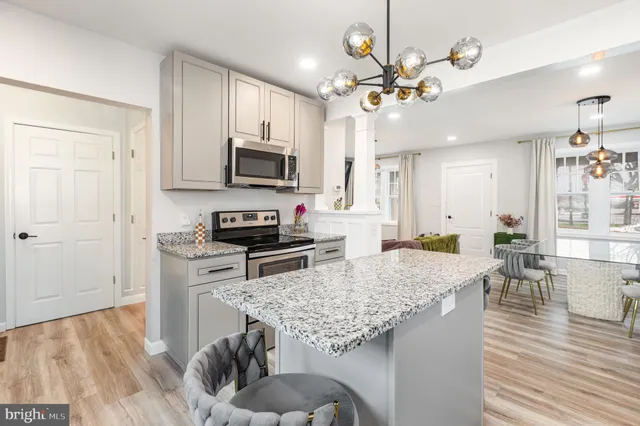 a kitchen with kitchen island granite countertop a stove top oven a sink a dining table and chairs with wooden floor