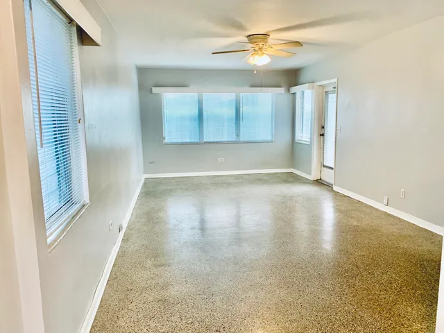 an empty room with wooden floor fan and windows