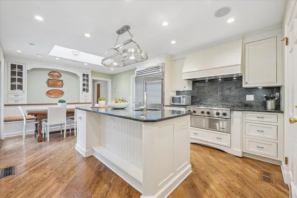a kitchen with stainless steel appliances kitchen island granite countertop a stove top oven a sink dishwasher and a dining table with wooden floor