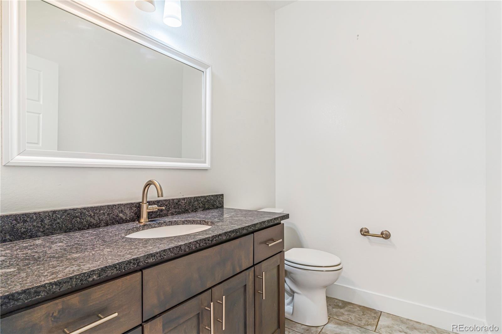 497 Valley Way Bennett, CO 80102 - Photo 13 of 37 a bathroom with a granite countertop sink a toilet and a mirror