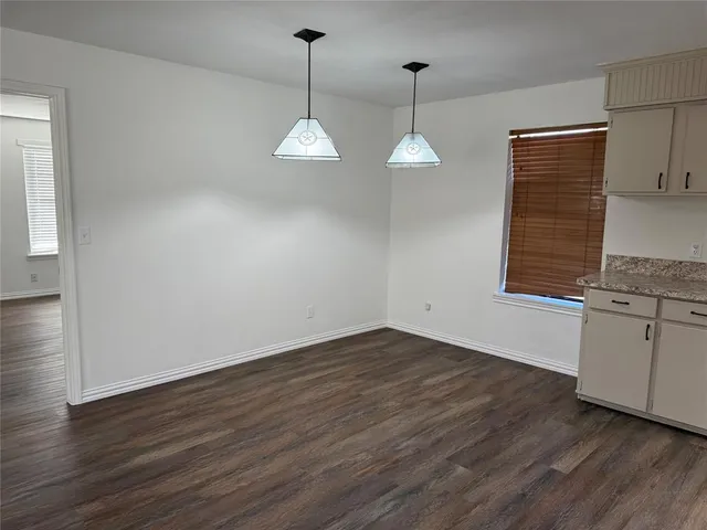 an empty room with wooden floor ceiling fan and kitchen view