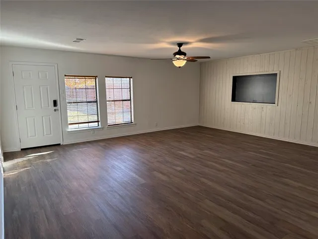 an empty room with wooden floor chandelier fan and windows