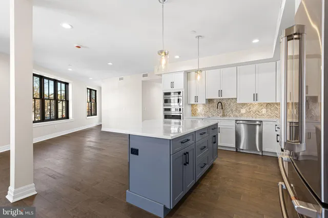 a kitchen with stainless steel appliances granite countertop a stove a sink a refrigerator and white cabinets with wooden floor