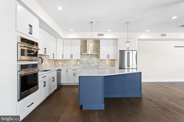 a kitchen with stainless steel appliances granite countertop a sink a stove a refrigerator and island with wooden floor