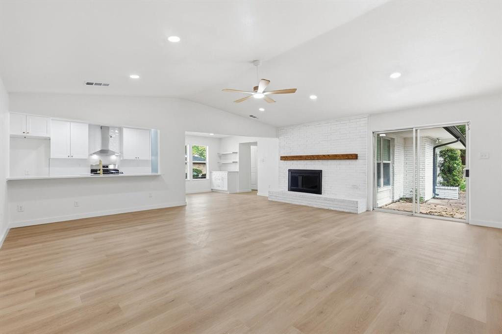 5940 Hunters View Lane Dallas, TX 75232 - Photo 1 of 24 Unfurnished living room featuring lofted ceiling, a brick fireplace, light wood-style floors, recessed lighting, and a ceiling fan