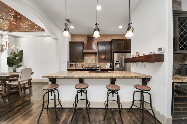 a kitchen with stainless steel appliances kitchen island granite countertop a dining table chairs and a refrigerator