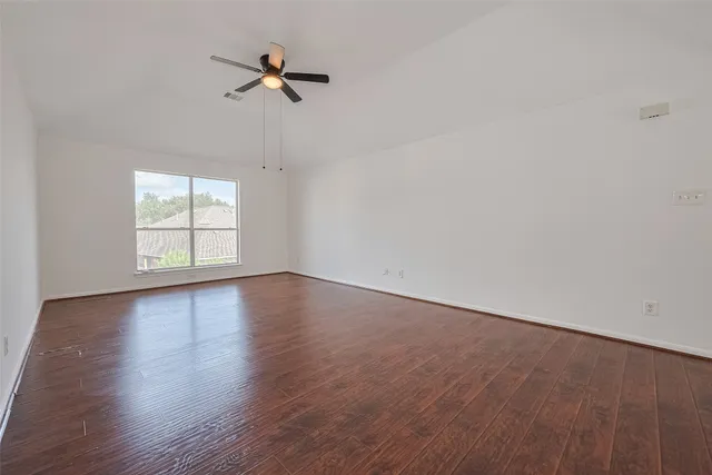 an empty room with wooden floor fan and windows