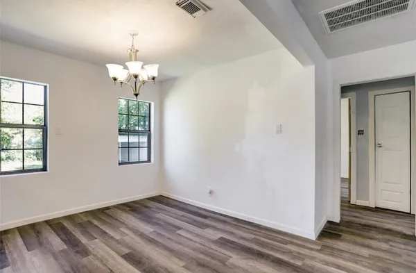 an empty room with wooden floor chandelier and windows