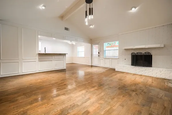 a view of empty room with wooden floor and kitchen