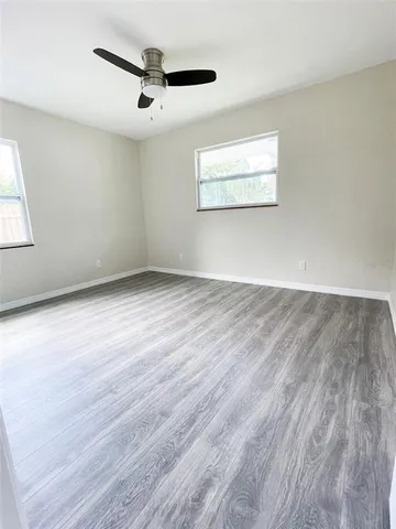 an empty room with wooden floor ceiling fan and windows
