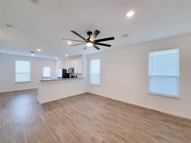 a view of an empty room with wooden floor and a ceiling fan