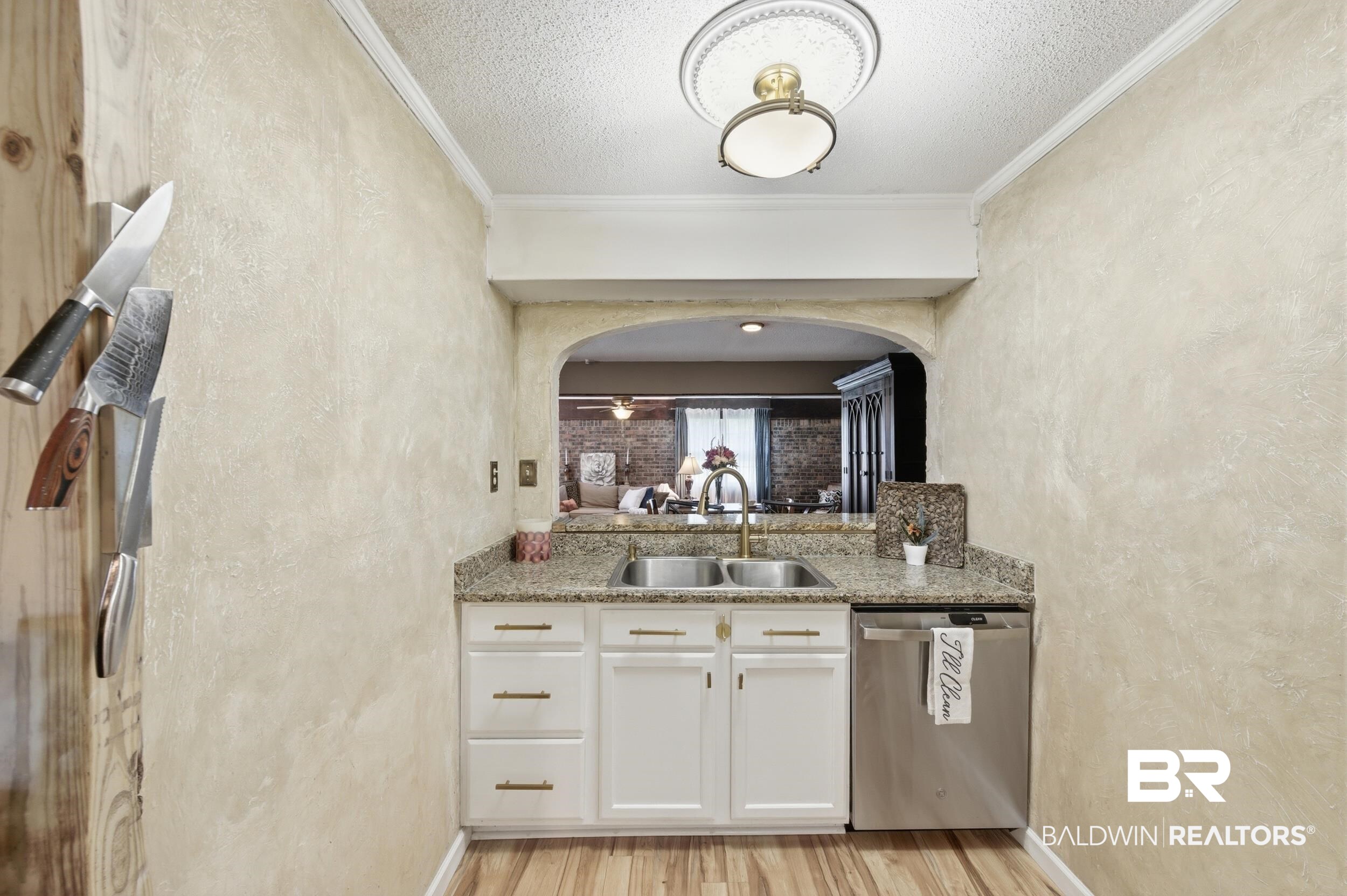 51620 Robert White Road Bay Minette, AL 36507 - Photo 35 of 81 Kitchen pass-through featuring an arched opening, granite-style countertop, dual stainless-steel sink with a brass-finish faucet, white cabinetry with brass-finish hardware, and a stainless steel dishwasher