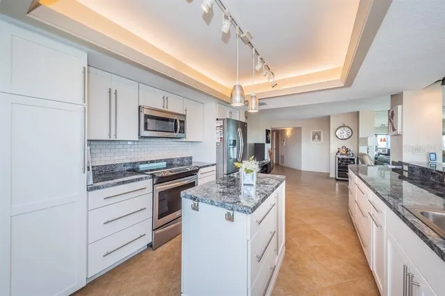 a large white kitchen with stainless steel appliances granite countertop a stove and a sink