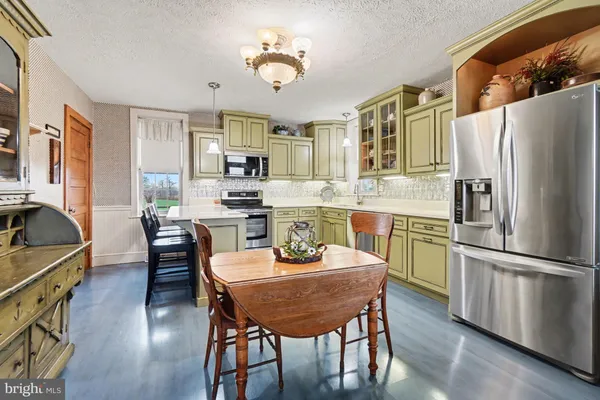 a kitchen with stainless steel appliances granite countertop a dining table chairs refrigerator and cabinets